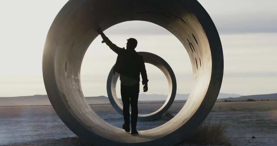 A man walking through a large section of pipe with his hand up touching the top
