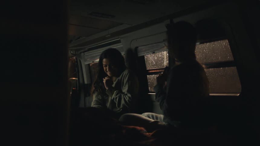 Two girls laugh in a van at night
