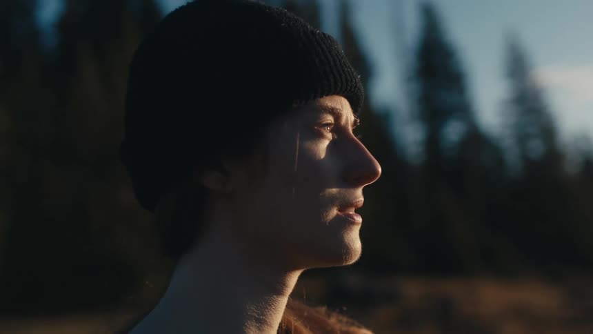 A woman wearing a knit cap is standing outside as the sun shines on her face