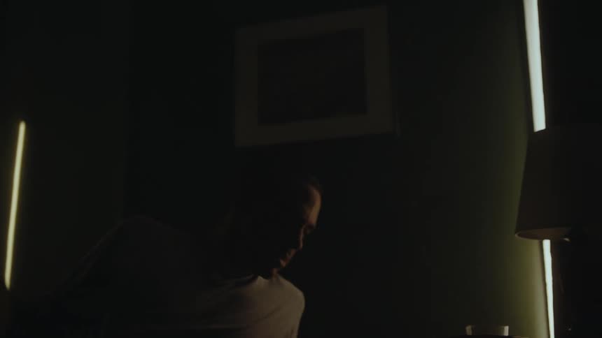 Man turns off alarm clock before getting out of bed and opening curtains to let in sunlight