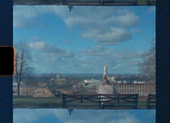 Vintage film of a man sitting on a park bench and looking towards the city skyline with a large monument