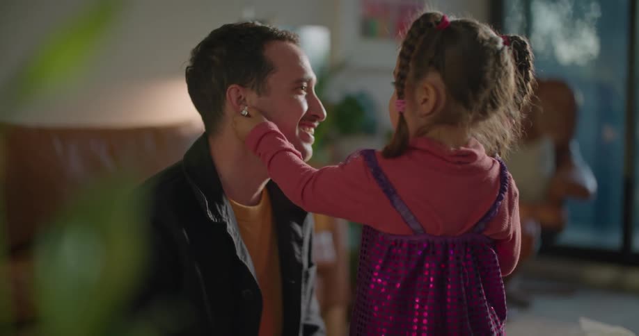 A man is in a living room playing with a little girl and she is putting an earring on him