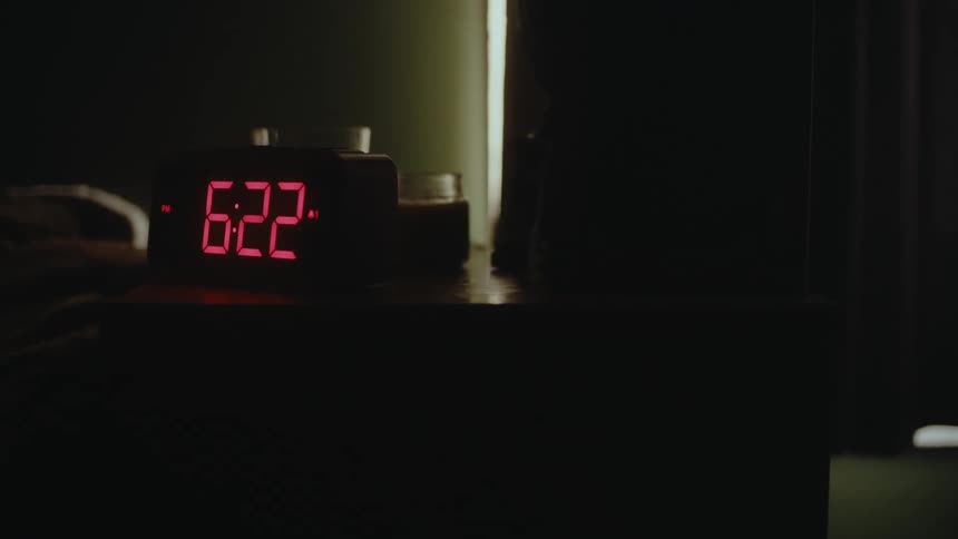 Digital alarm clock in dark bedroom near curtained window advances the minutes