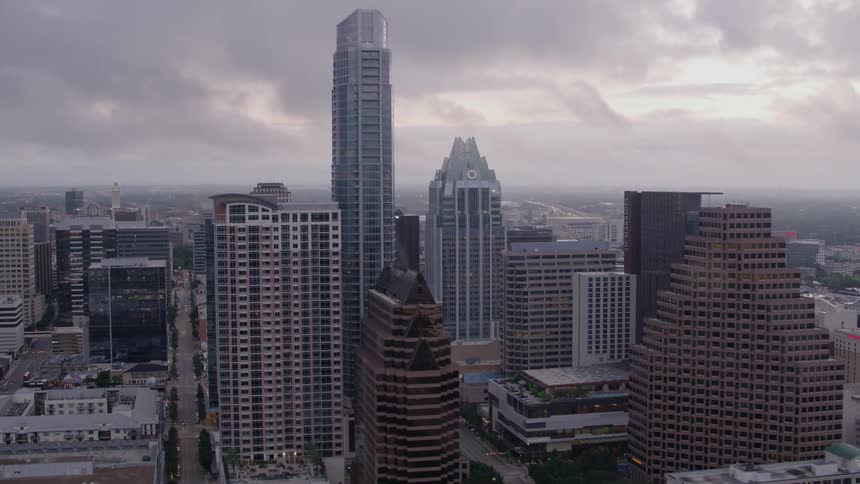 Tall buildings and skyscrapers under a cloudy sky as automobiles travel on a downtown street