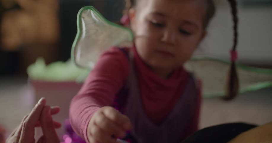 A little girl wearing fairy wings places a sticker on dads face