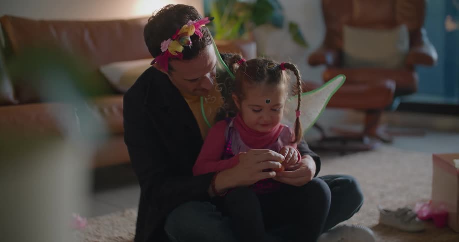 A man plays with a small girl sitting in his lap in the living room of a house during the day