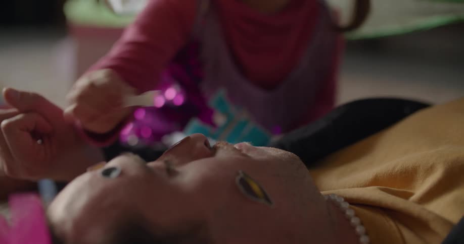 A dad growls playfully as his daughter in fairy wings places stickers on his face