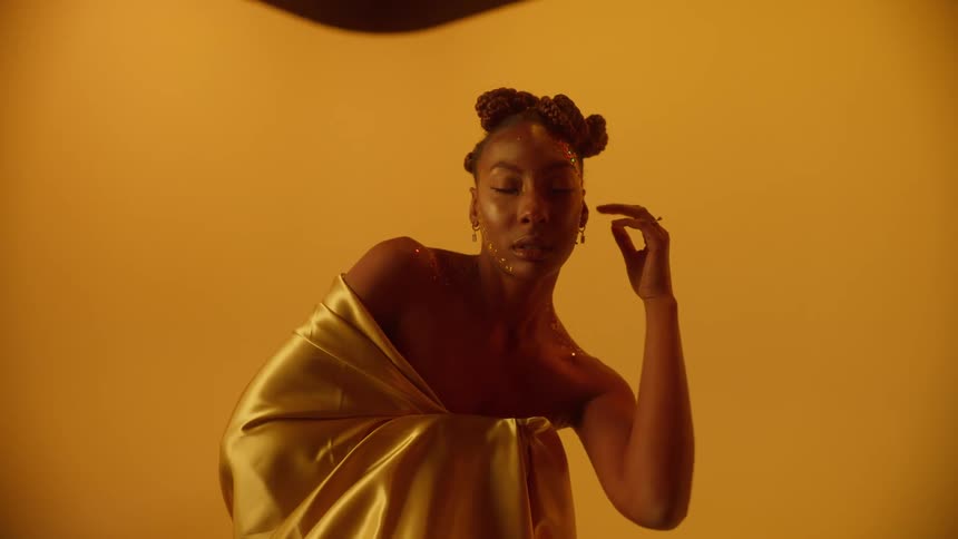 Young beautiful woman wearing golden clothes covered in glitter waving her hands in front of a yellow background