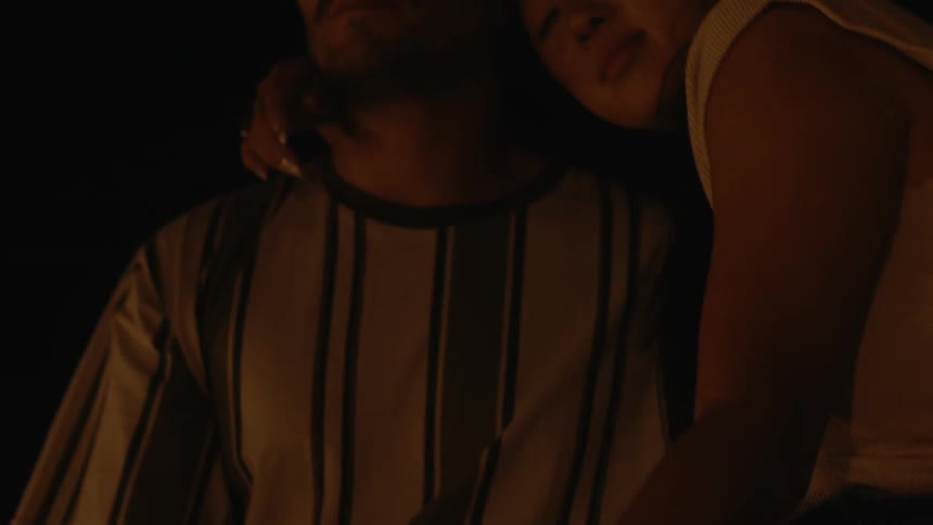Woman reclines her head on the shoulder of a handsome man sitting near a campfire at night