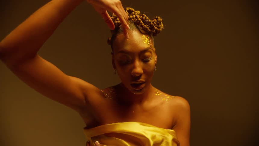 A black woman with glitter on her face is posing and modeling