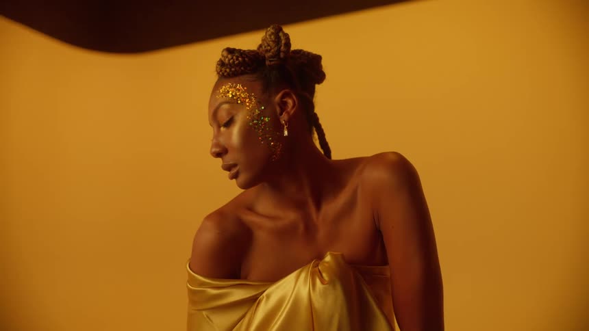 Black model with glitter on face posing against a yellow backdrop