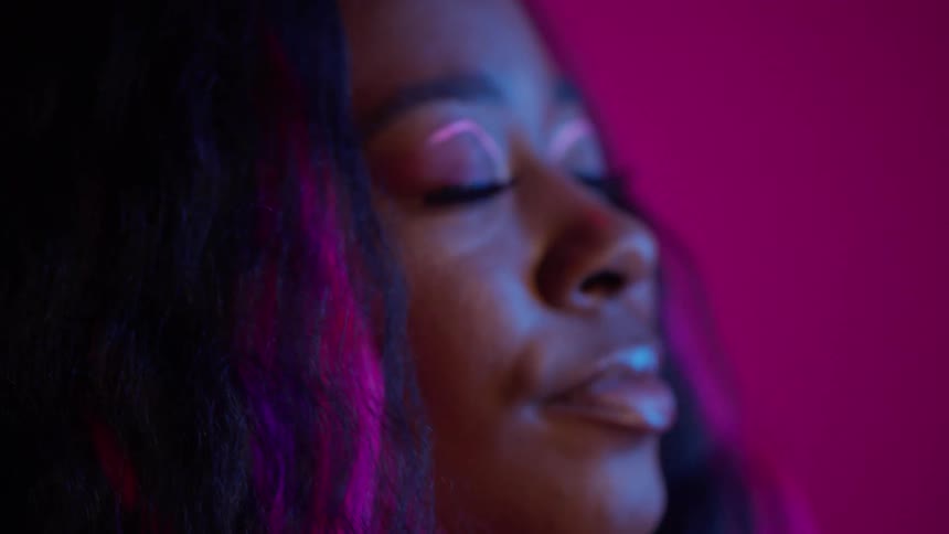 Close up of the face of a young woman with colorful makeup and hair dancing with eyes closed