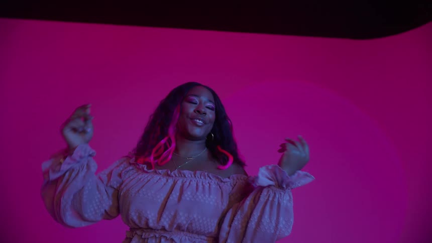 A black woman is dancing in a room with hot pink walls
