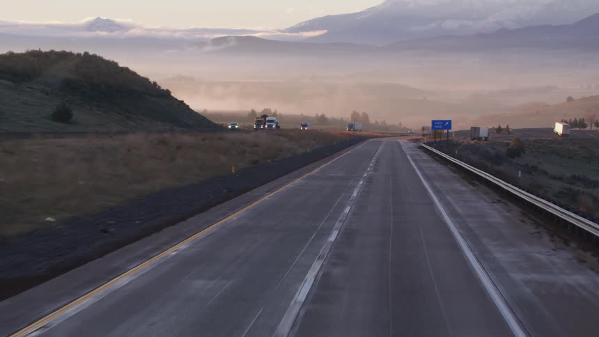 Traveling on a highway with many trucks passing on the other side and mountains in the distance
