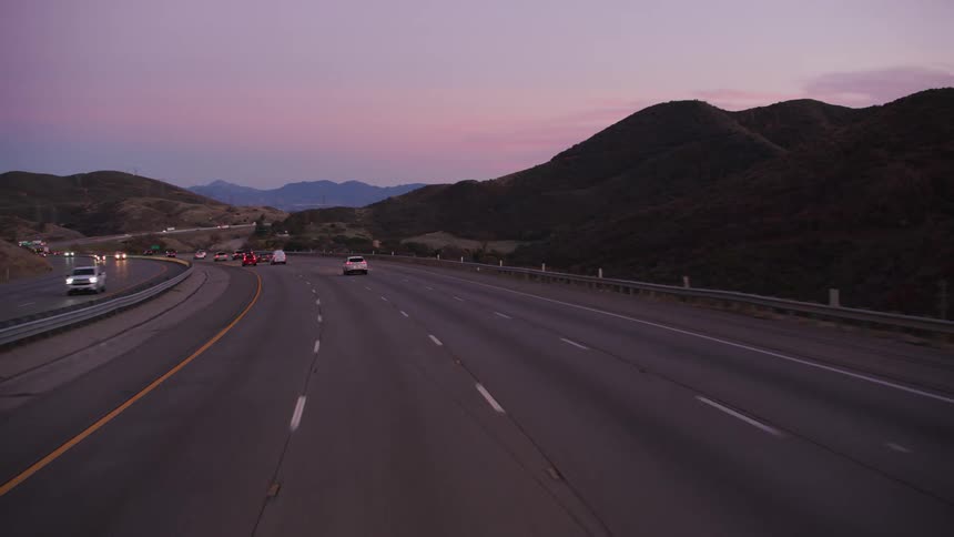 Traffic travels along a large freeway through the countryside in the evening