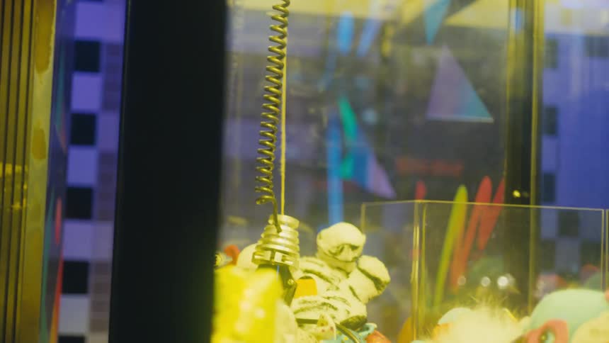 An elderly woman operates a crane game as an elderly man gives her advice