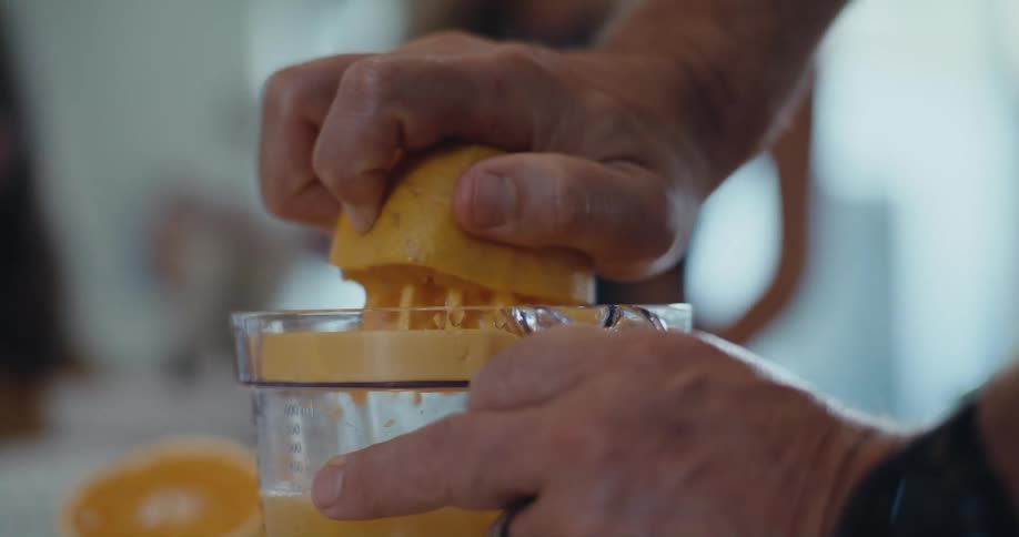 A man is making fresh squeezed orange juice and two people are watching
