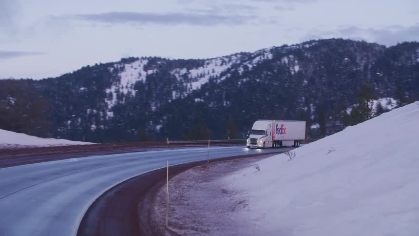 Aerial view of a white fedex truck driving on a mountain road in the winter at evening