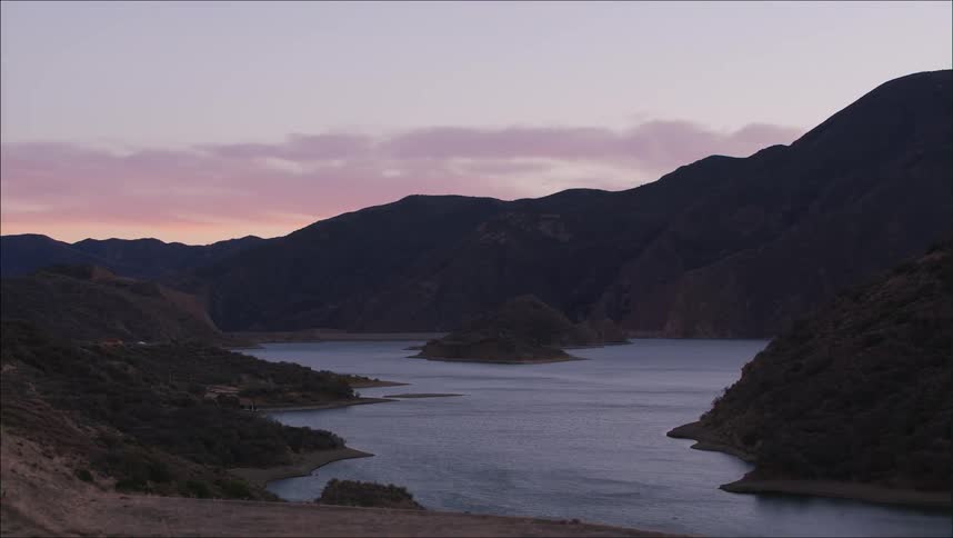 Placid lake near a road next to a mountain range at evening