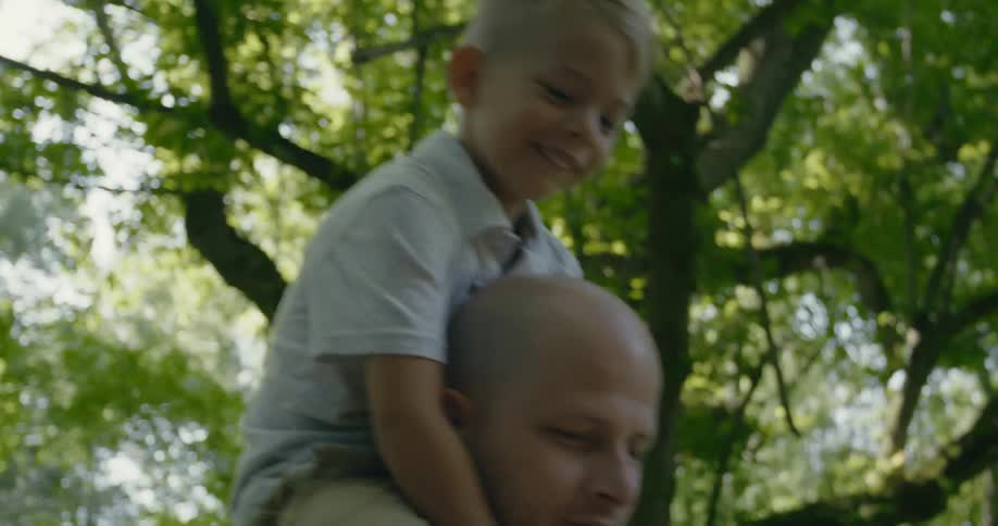 Father carries son on his shoulders while walking among trees