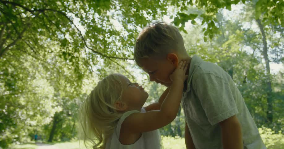A young girl kisses an older boy on the nose as they stand outdoors during the day
