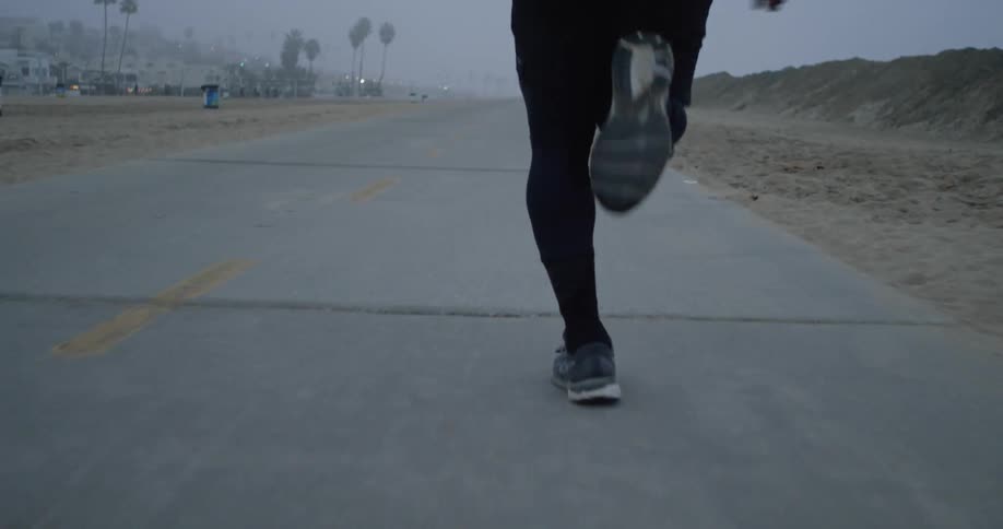 A runner jogging on a road with palm trees and lights visible through the fog
