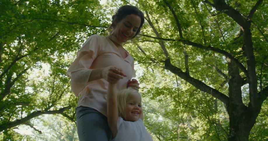 A mother and daughter smile and laugh as they dance under trees