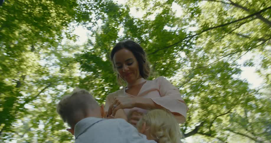 A mom smiles as she stands in the yard under the trees playing with her children