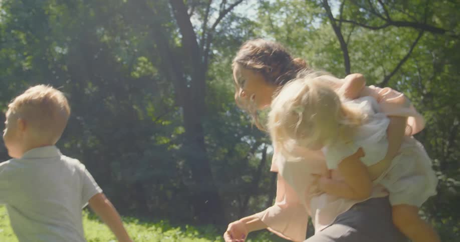 Mother carries daughter as she follows son through sloping field bordered by old wooden fence