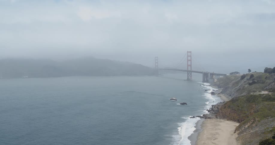 Heavy fog sits over a bridge that runs over the ocean