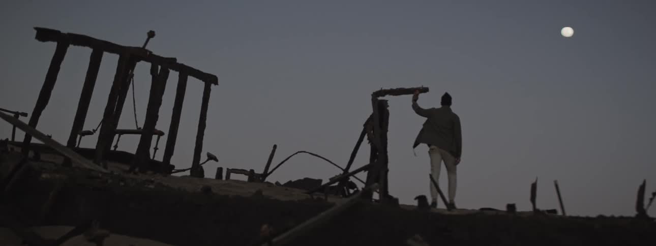 Man standing on the ruins of a shipwreck looking at a full moon