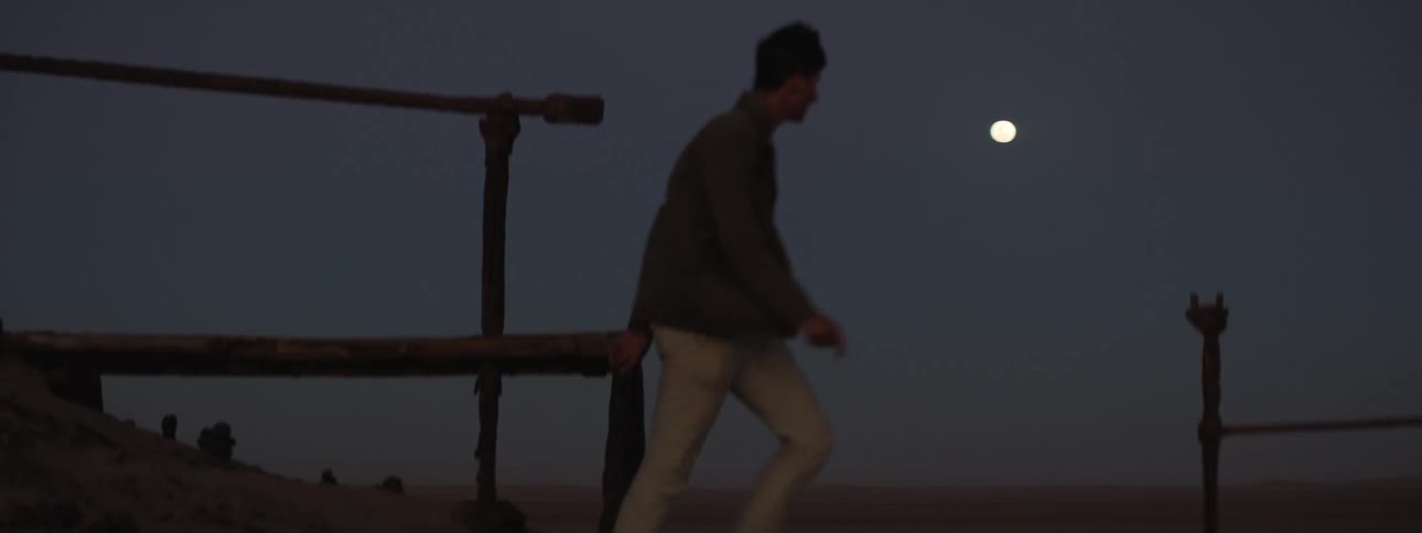 Young man walks along shipwreck at night with moonlit sky