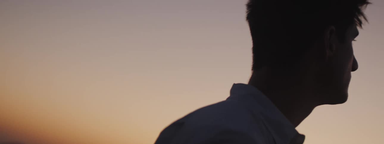 Young man stands against mountains in background under a red tinted sky