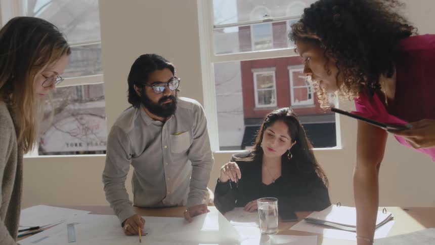 Workers discuss project documents standing around meeting table