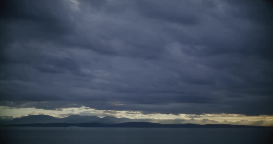 Dark clouds hang low in the sky as a boat sails across the water