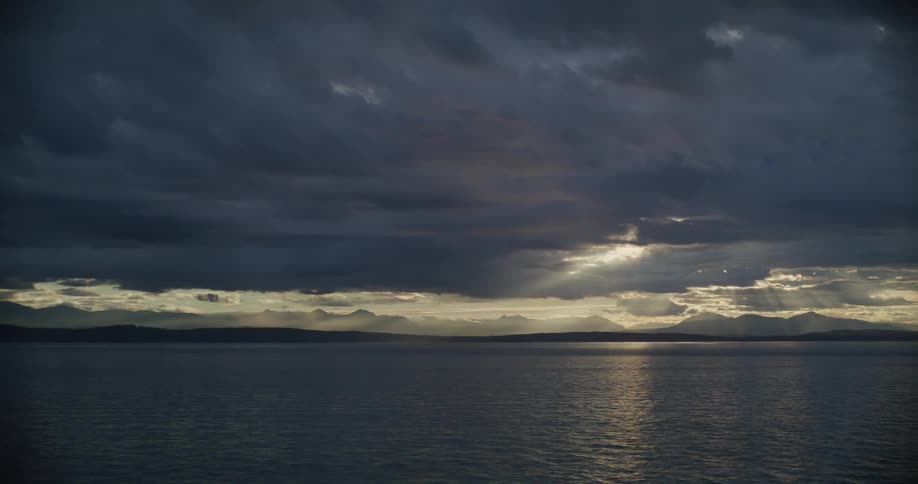 The sun peeks through dense clouds to shine down on the vast sea below