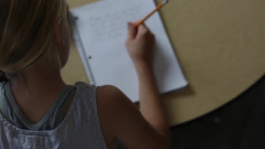 A girl is writing in a notebook with a pencil
