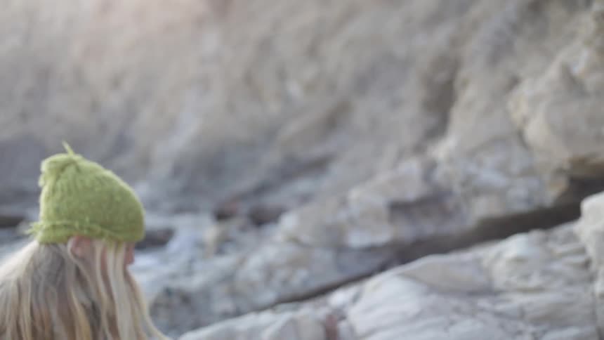 A girl is hiking along rocks with a stick