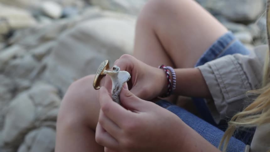 A woman examines a shell on some rocks