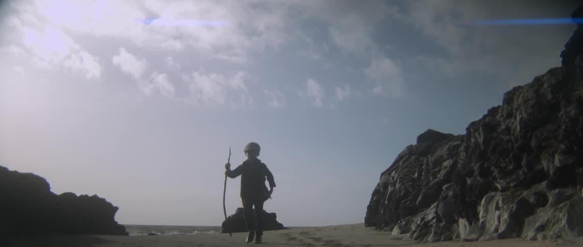 A young boy hikes on the beach with a walking stick