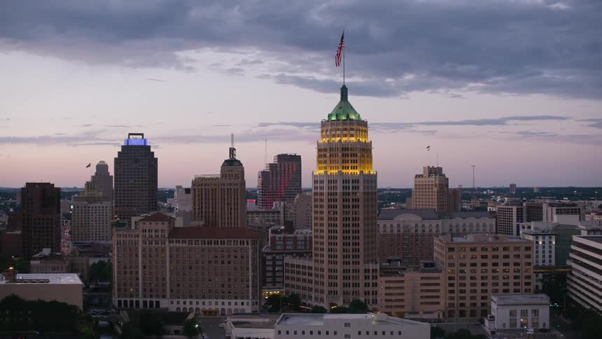 Flag on flagpole stands on building in downtown near river under a red sky