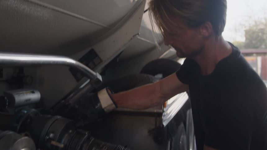 A man is attaching a hose to a truck with a large tank on it