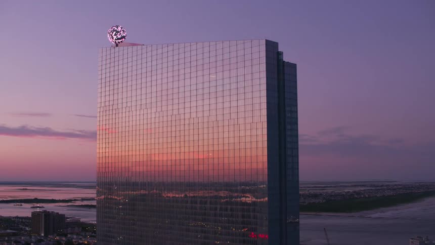 Reflective facade of skyscraper sitting near the water reflects other buildings and the red sky