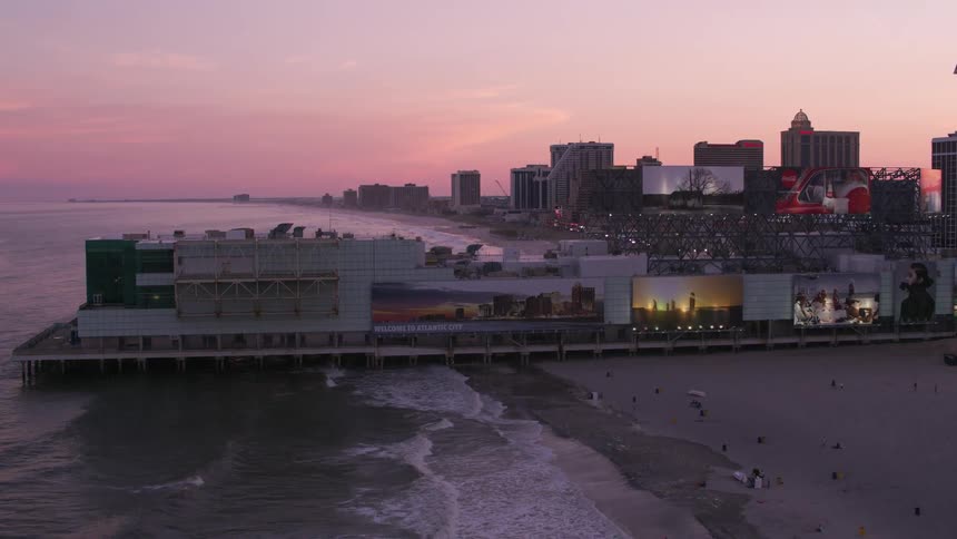 Beach goers move around beach near pier and buildings