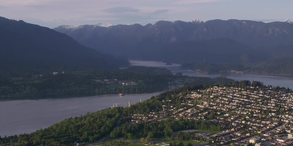 A small town of homes on a hillside near water and mountain ridges