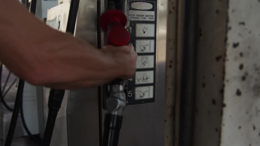 A man puts a fuel nozzle back on the gas pump