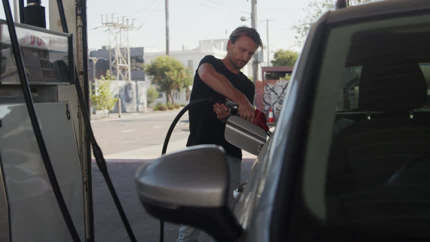 Man in a black shirt pumping gas at a gas station in the city