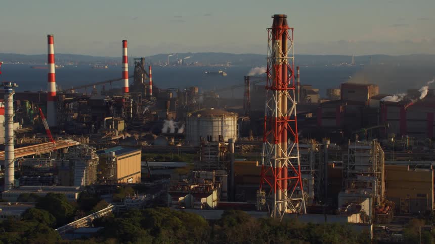 Smoke billows from smoke stacks near the waterfront lined with factories and plants