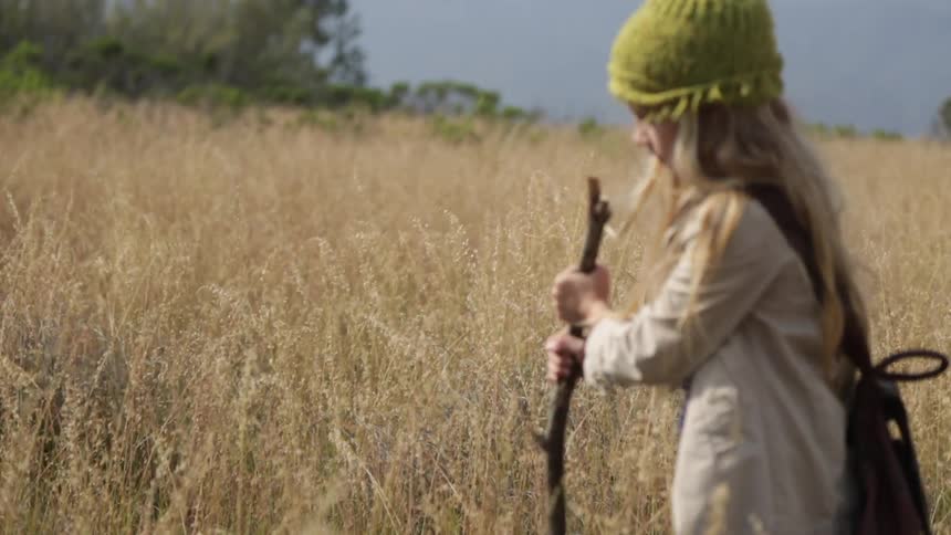 Child walks through tall grass carrying a stick