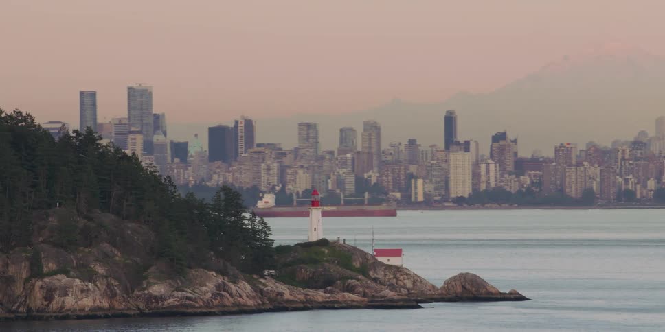 A light house on the shore with boats in the water and a city skyline in the distance